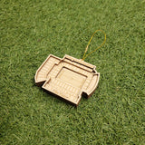 A wooden ornament resembling a stadium or sports arena is lying on a grassy surface.