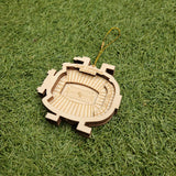 A wooden ornament resembling a football stadium is lying on a grassy surface.