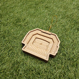 A wooden ornament resembling a football stadium is placed on a grassy surface.