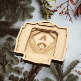 A wooden ornament shaped like a baseball stadium, with the name "Chase Field" displayed on it, is hanging among pine branches and greenery.