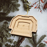 A wooden ornament resembling a stadium is hanging from a string, surrounded by pine branches and greenery.