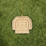A wooden ornament resembling a football stadium is placed on a grassy surface.
