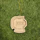 A wooden ornament depicting a football stadium is placed on a grassy surface.
