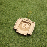 A wooden ornament with a baseball design rests on a grassy surface.