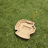A wooden ornament resembling a stadium is lying on a grassy surface.